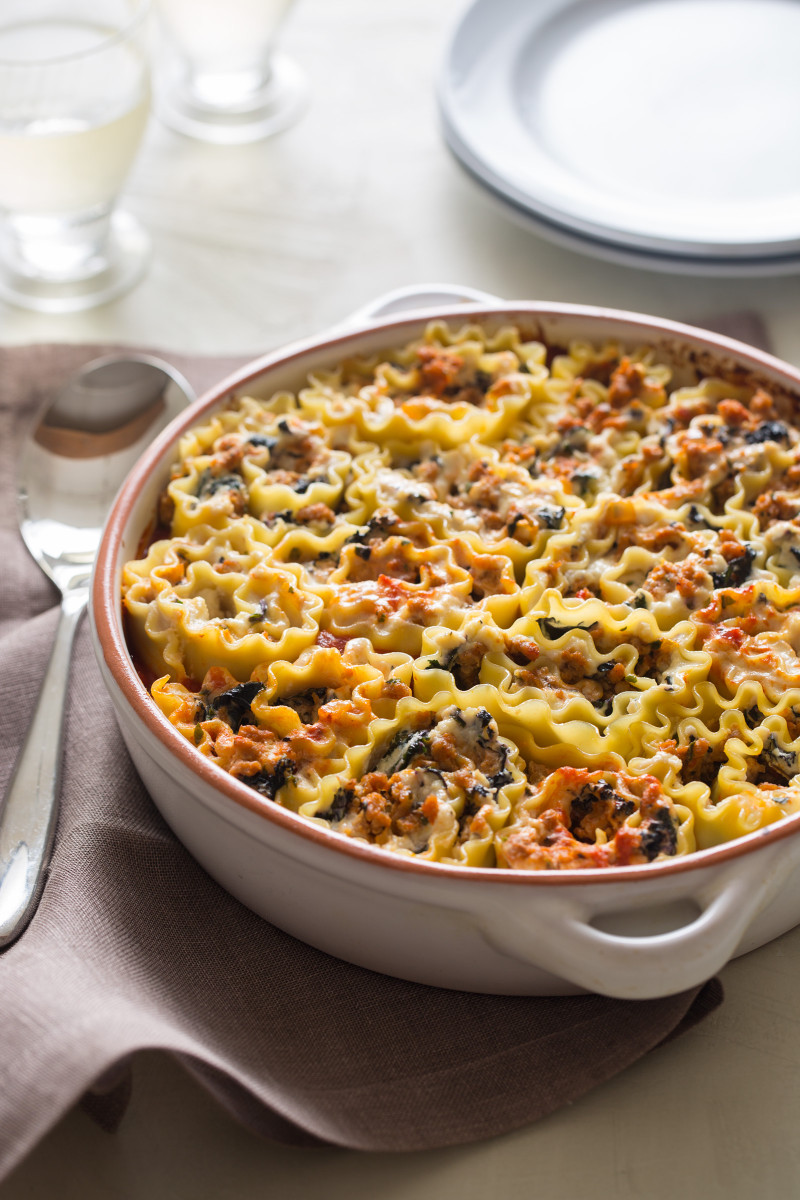 A baking dish full of lasagna roll ups with a spoon.