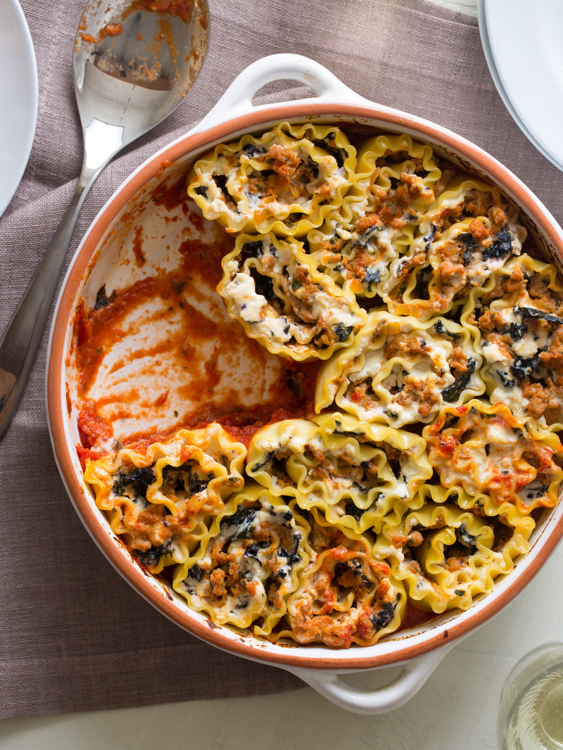 A baking dish full of lasagna roll ups with a portion taken out.