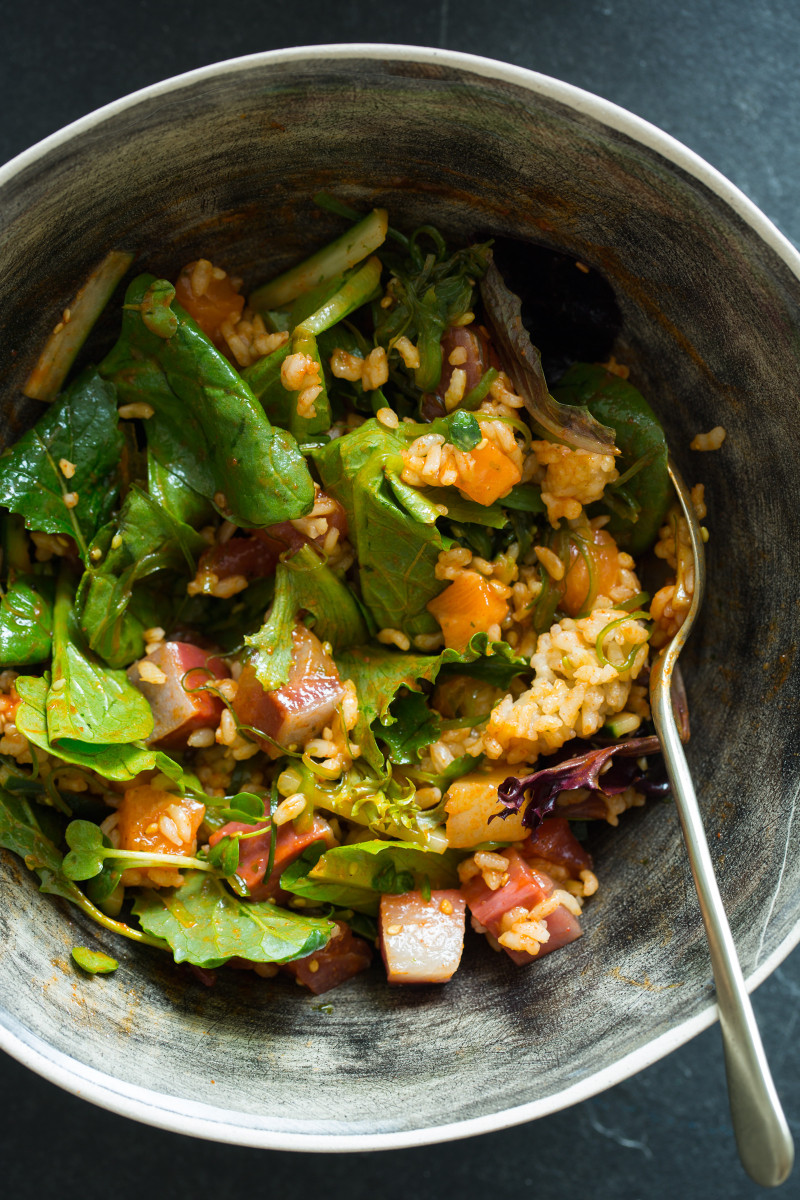 A close up of Korean spicy sashimi salad mixed up in a bowl with a spoon.