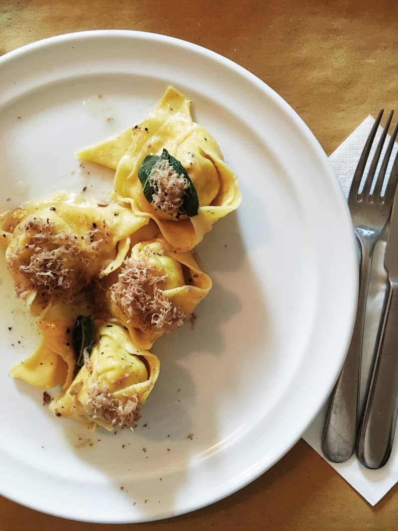 A plate of pasta with freshly shaved white truffle next to a fork and knife.