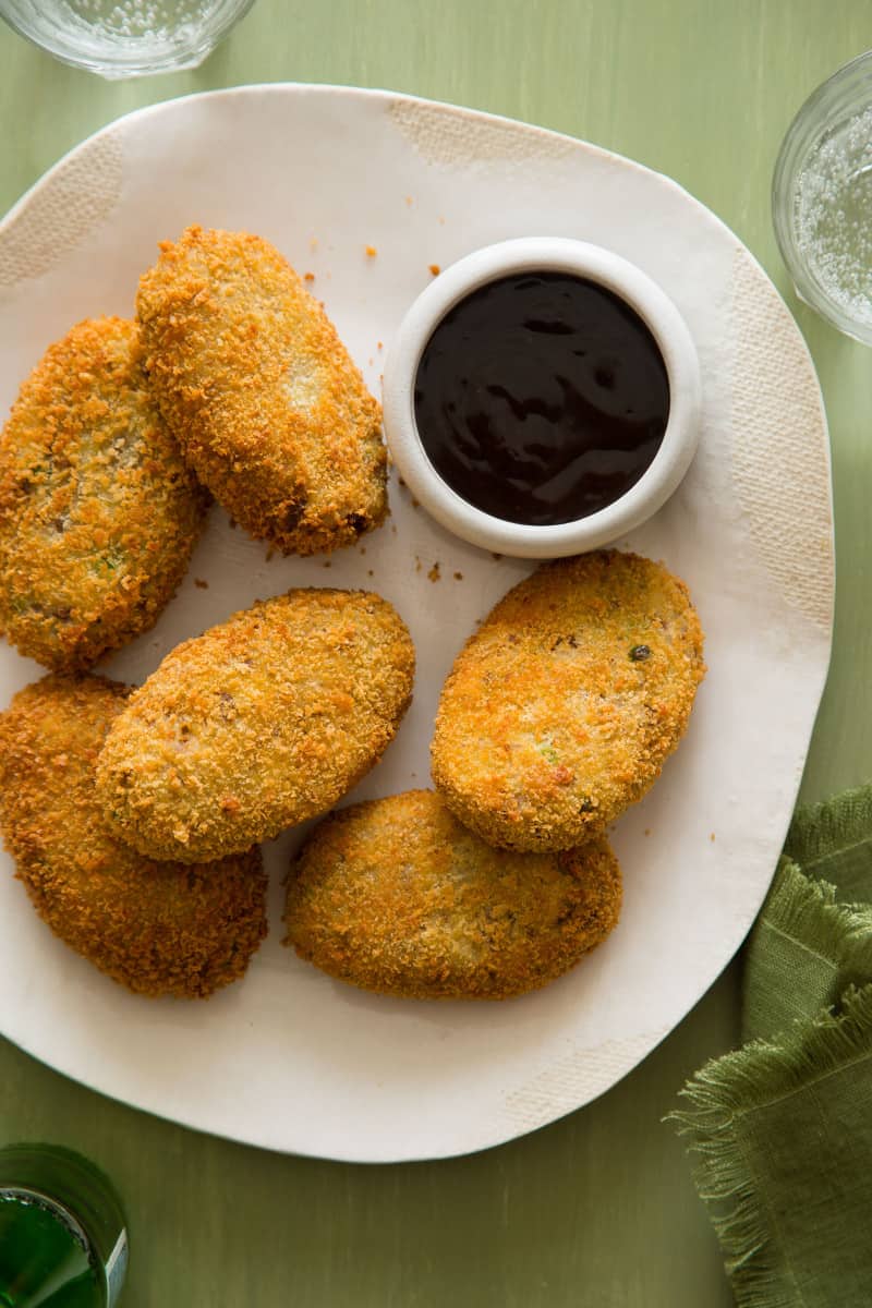 Korokke on a plate next to a ramekin of sauce.