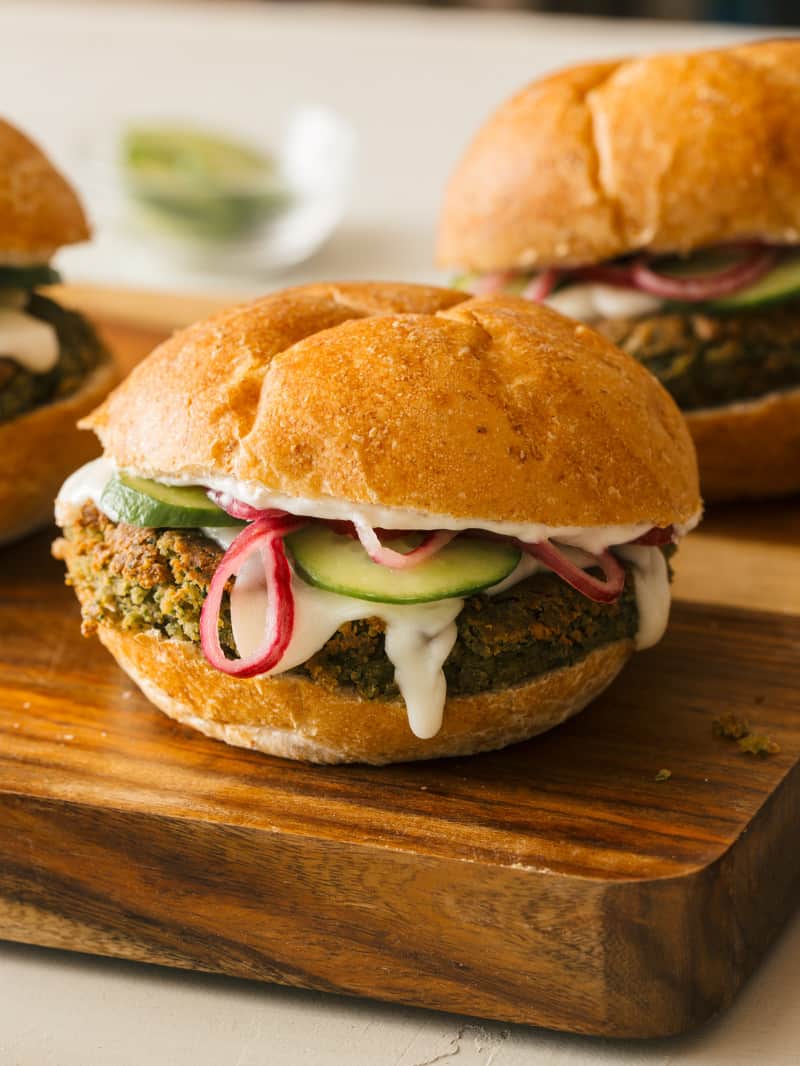 A close up of falafel burgers with veggies and sauce on a cutting board.