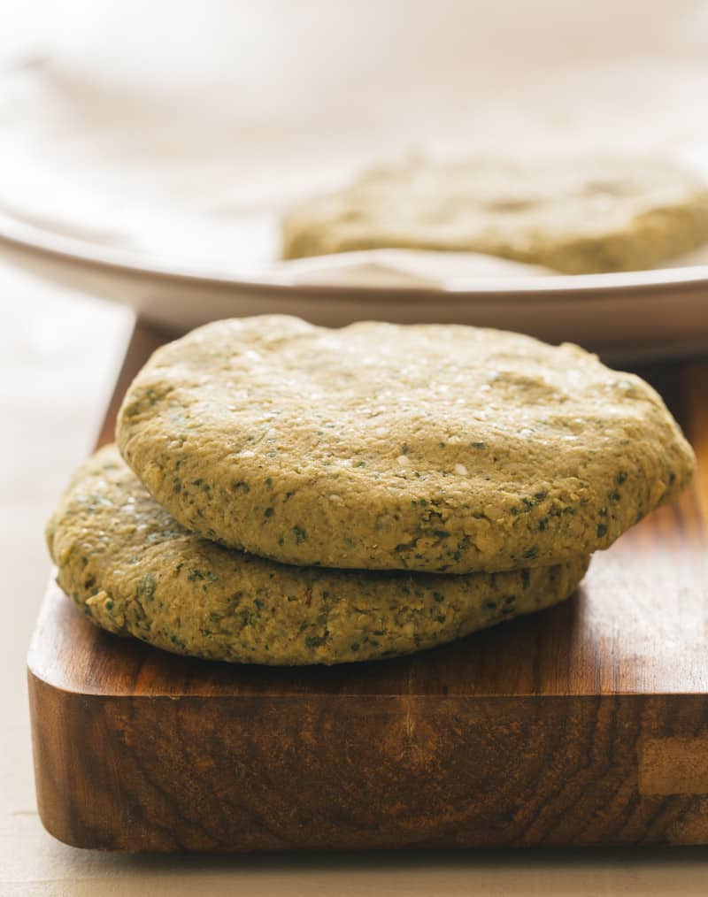 A close up of falafel burger patties on a wooden cutting board and a plate.