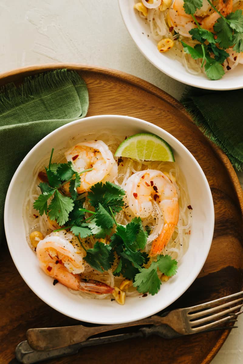 A bowl of yum wood sen with shrimp garnished on a wooden tray.