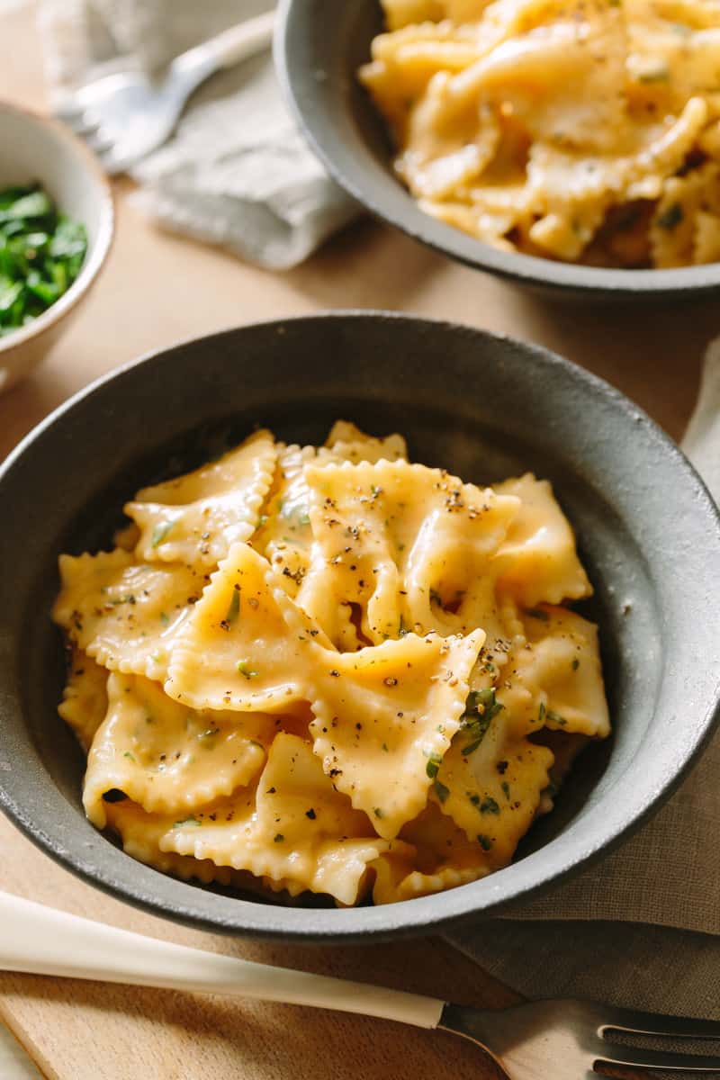 Farfalle with creamy white bean and roasted garlic sauce in black bowls.