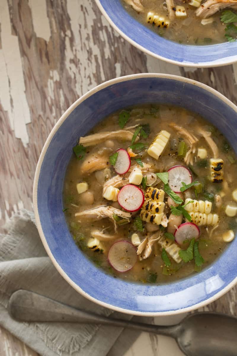 A close up of spicy white bean chili with shredded chicken in a blue bowl.