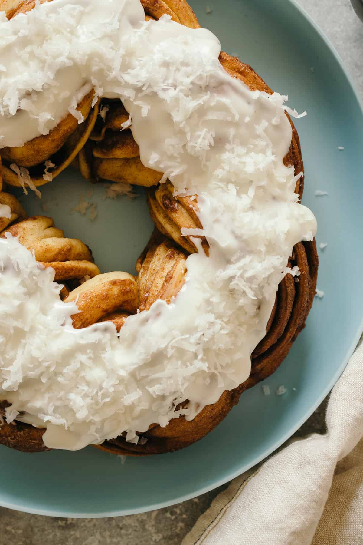 Brown butter braided cinnamon roll cake topped with shredded coconut on a plate.