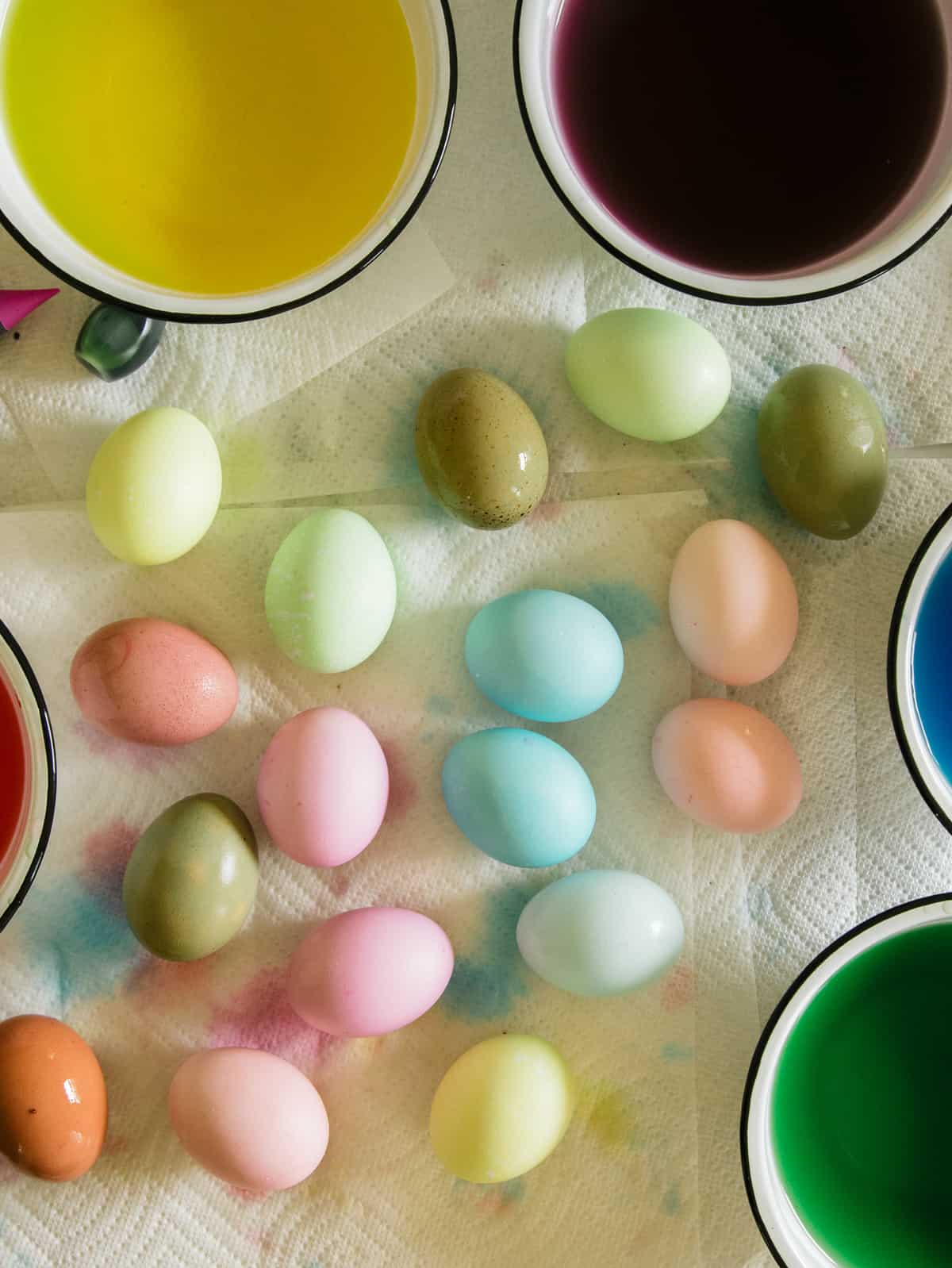 Dyed Easter eggs in a variety of colors on paper towels next to bowls of dye.