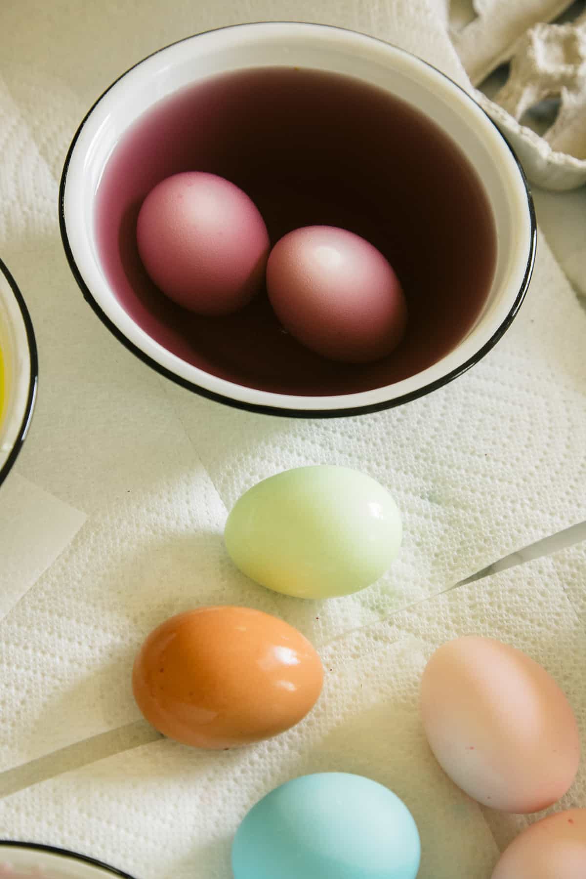 A bowl of dye with eggs in it next to eggs on a paper towel.