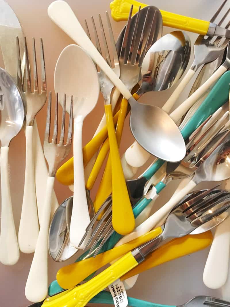 A close up of white, yellow, and teal handled flatware.