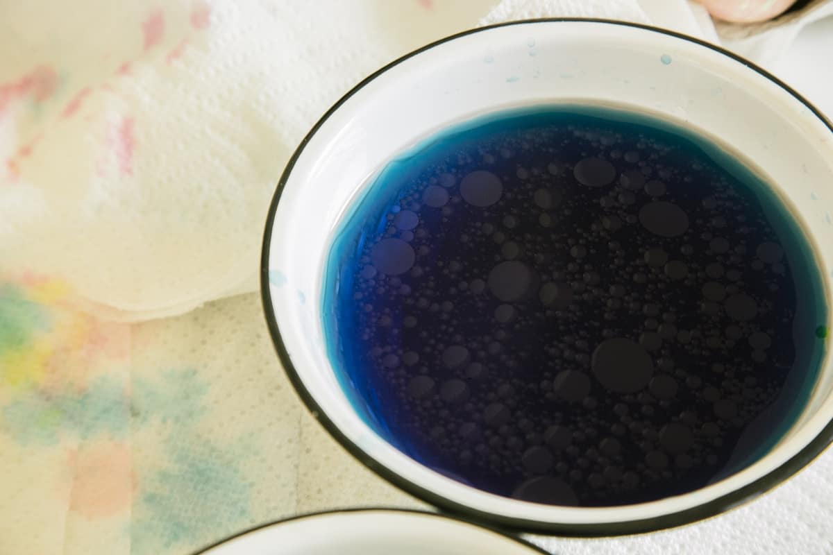 A white bowl of dark blue egg dye on top of paper towels.