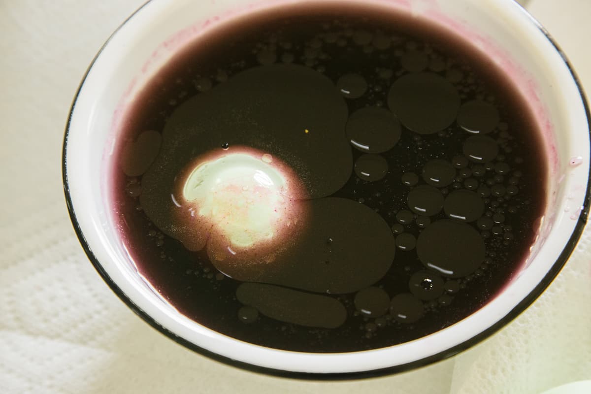 A close up of a bowl of dark egg dye with an egg in it.