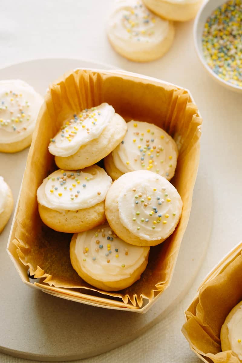 Soft and fluffy sugar cookies with vanilla frosting and sprinkles in a paper lined dish.