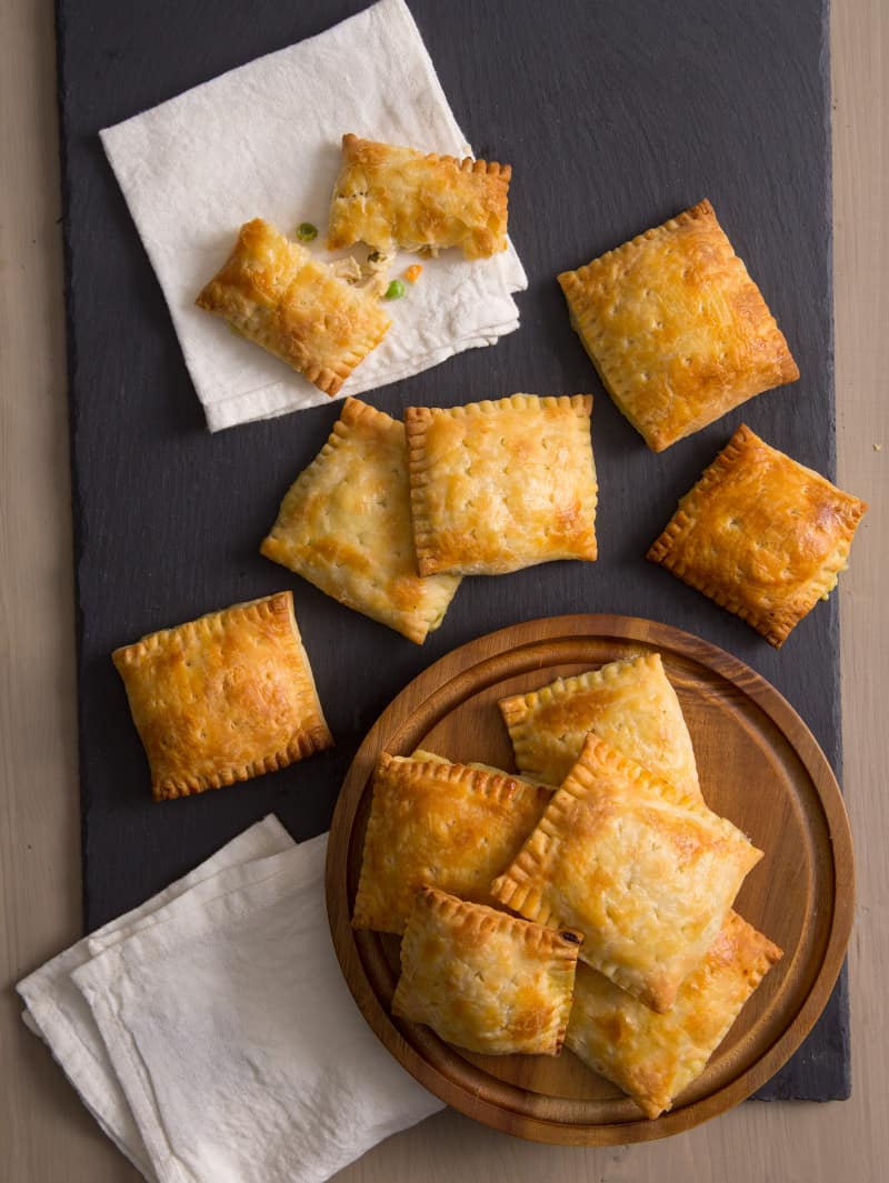 Several chicken pot pie hand pies on a dark board, a round wooden board and napkins.