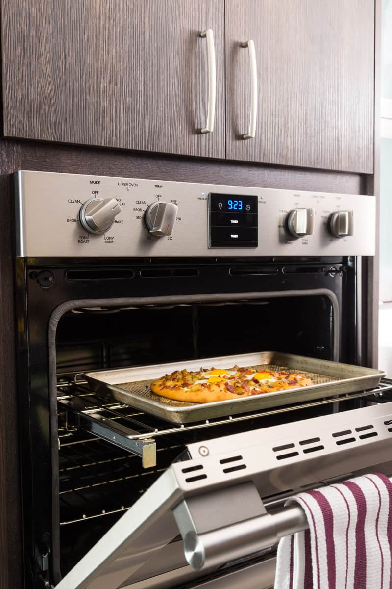 A finished breakfast pizza coming out of an oven.