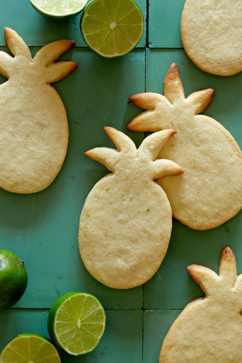 A close up of pineapple shaped lime sugar cookies with limes.