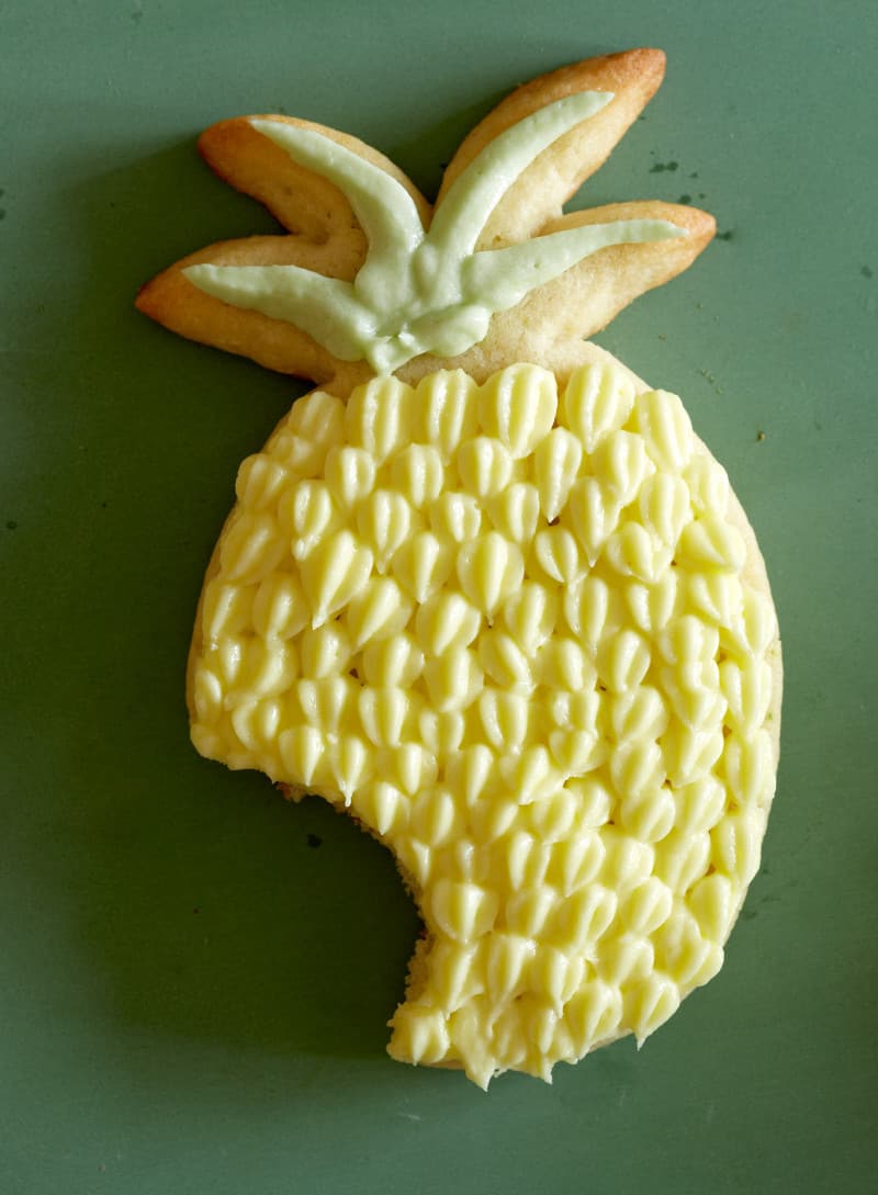 A pineapple shaped lime sugar cookies with pineapple buttercream with a bite taken out.