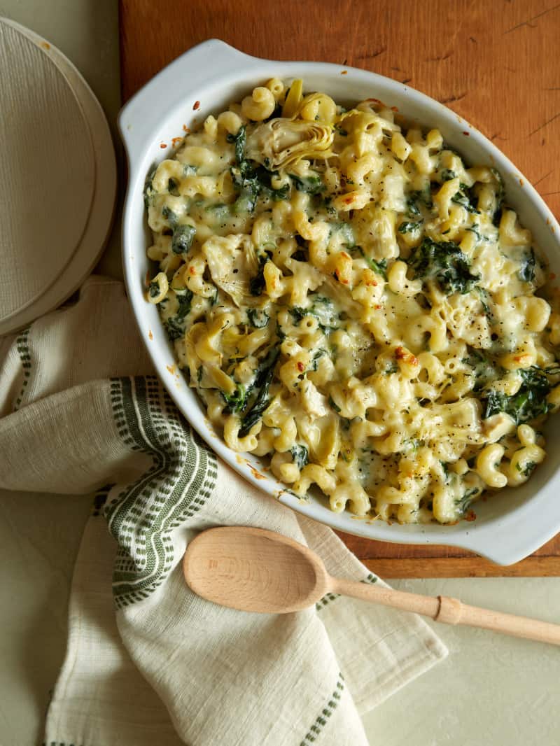 Spinach artichoke mac and cheese with plates, linens, and a wooden spoon.