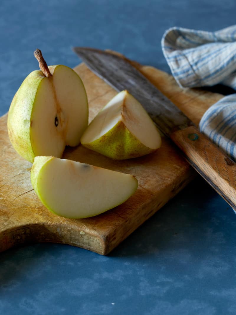 A sliced pear on a wooden cutting board with a tea towel and a knife.