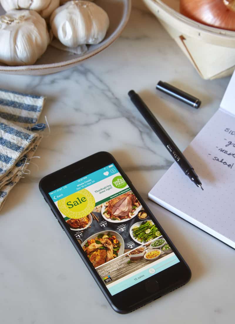 A phone next to a pen and paper list on a marble countertop.