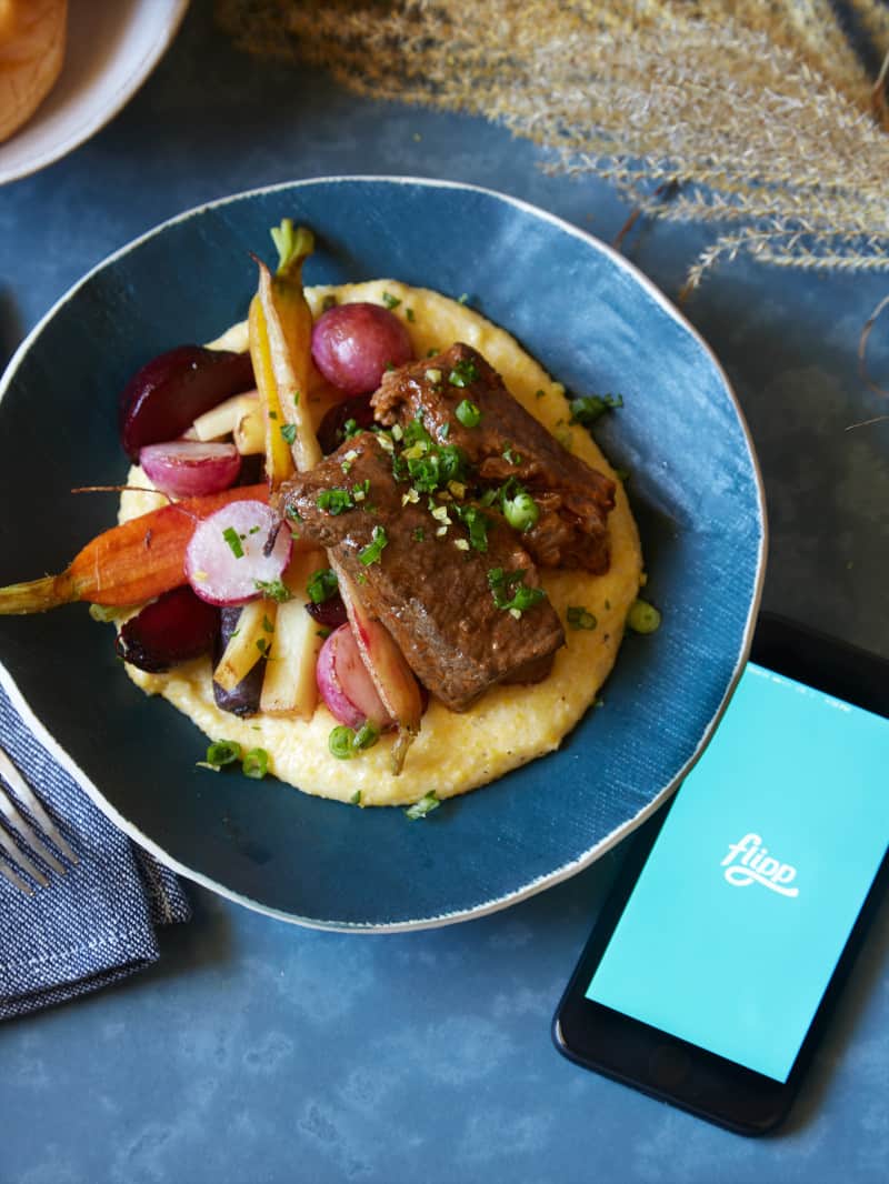 White wine braised short ribs with vegetables over white cheddar polenta next to a phone.