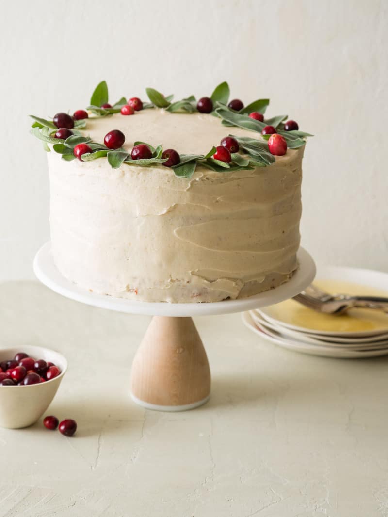 Apple cranberry cake with brown sugar buttercream decorated with fresh cranberries with plates and forks.