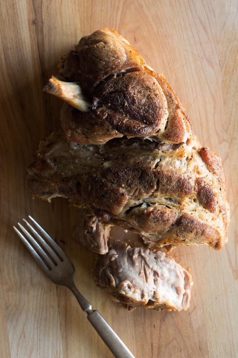 Milk braised pork shoulder with a fork on a wooden cutting board.