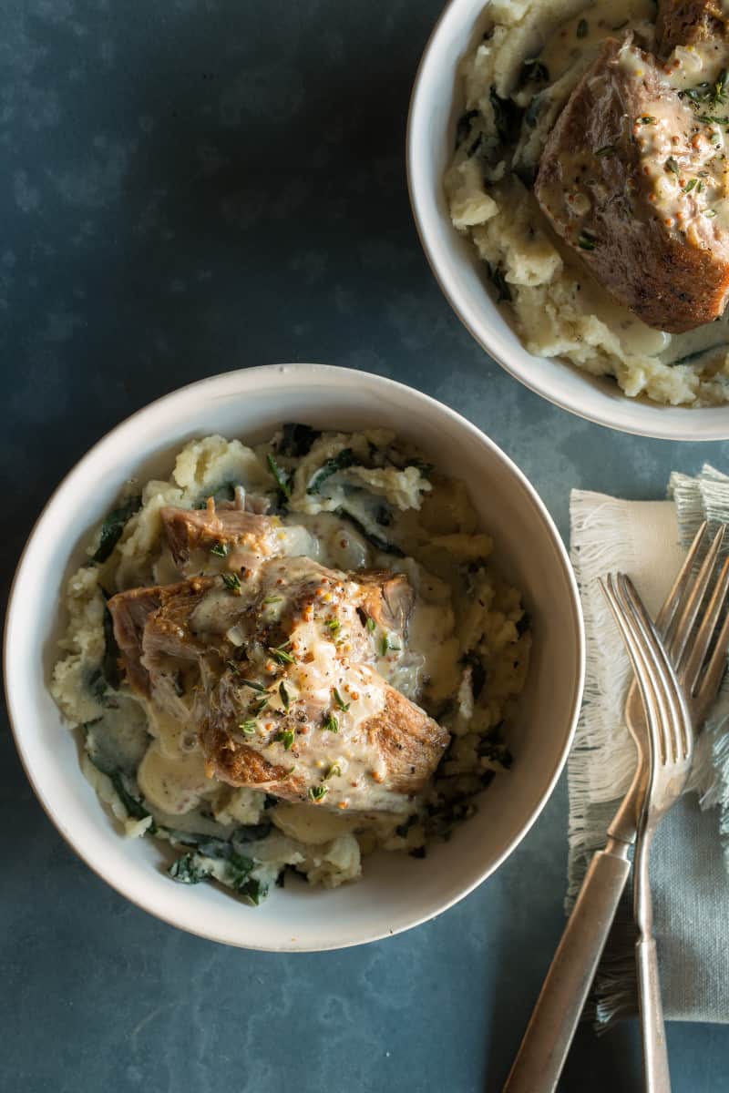 Bowls of milk braised pork shoulder over browned butter colcannon with forks.