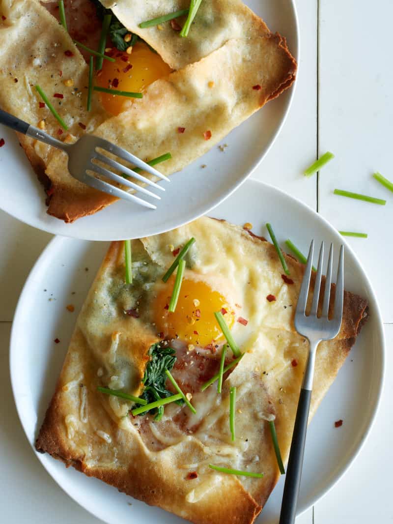 Plates of ham, spinach, and swiss stuffed breakfast crepes with forks.