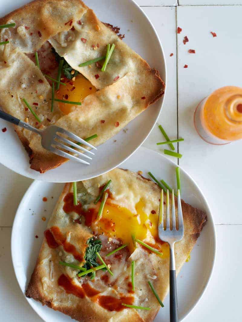 Plates of ham, spinach, and swiss stuffed breakfast crepes with forks.