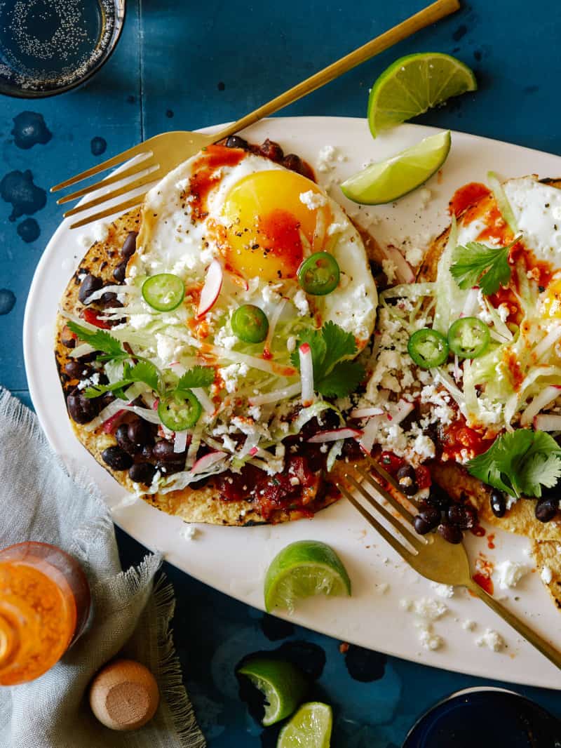 A plate of huevos rancheros with black beans and chipotle salsa with forks.