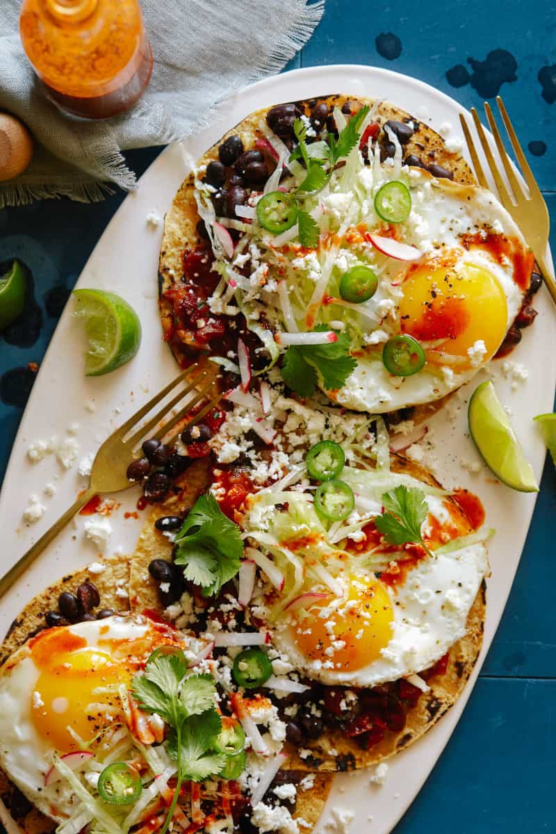 A plate of huevos rancheros with black beans and chipotle salsa with forks.