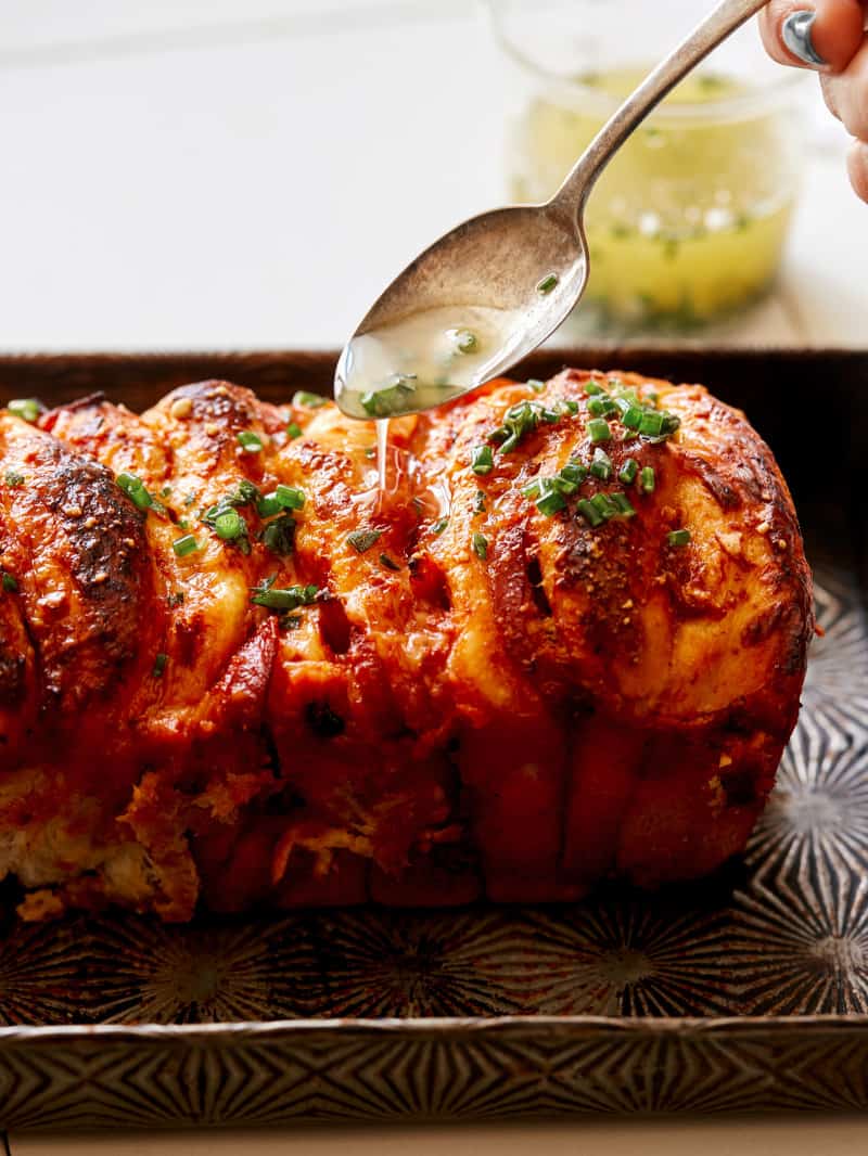 Pizza pull apart bread with a spoon drizzling garlic herb butter on top.