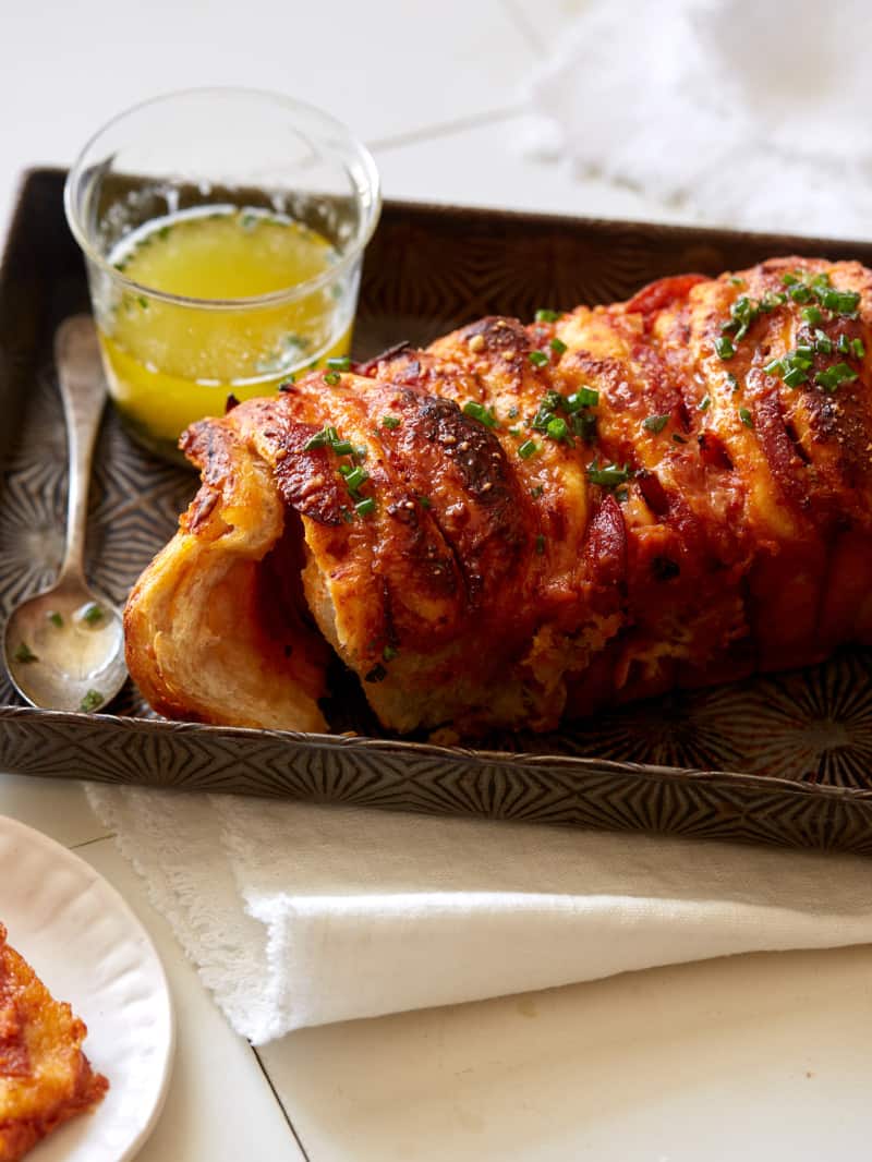 Pizza pull apart bread with a spoon drizzling garlic herb butter on top.