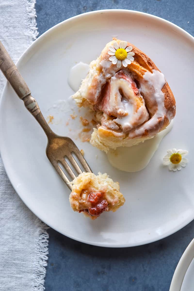 A piece of strawberry cinnamon rolls with chamomile and vanilla glaze and a fork.