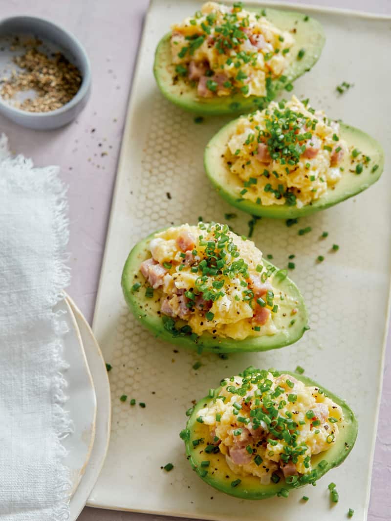 Breakfast scramble stuffed avocados on a plate with ramekin on the side.