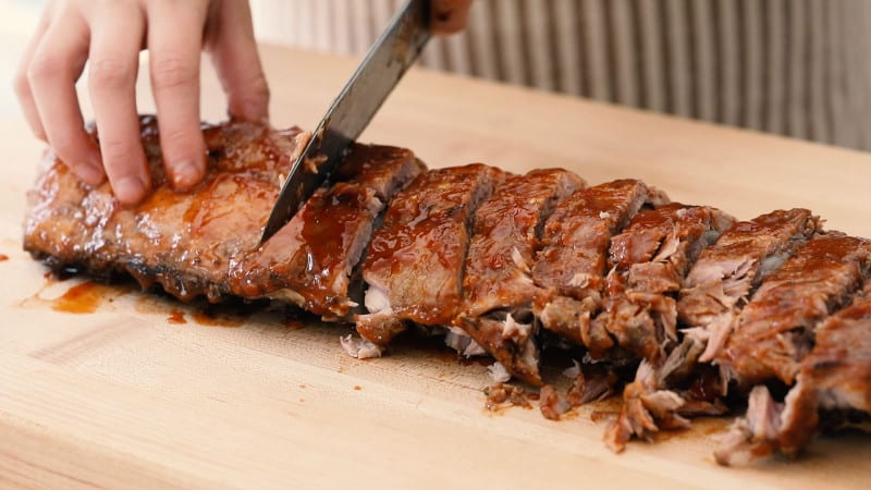 Baby back ribs being cut with a sharp knife.