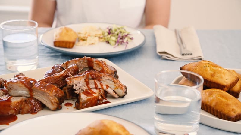 A plate of baby back ribs with a person waiting to be served.