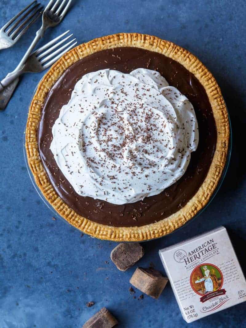 A whole chocolate cream pie with forks and chocolate.