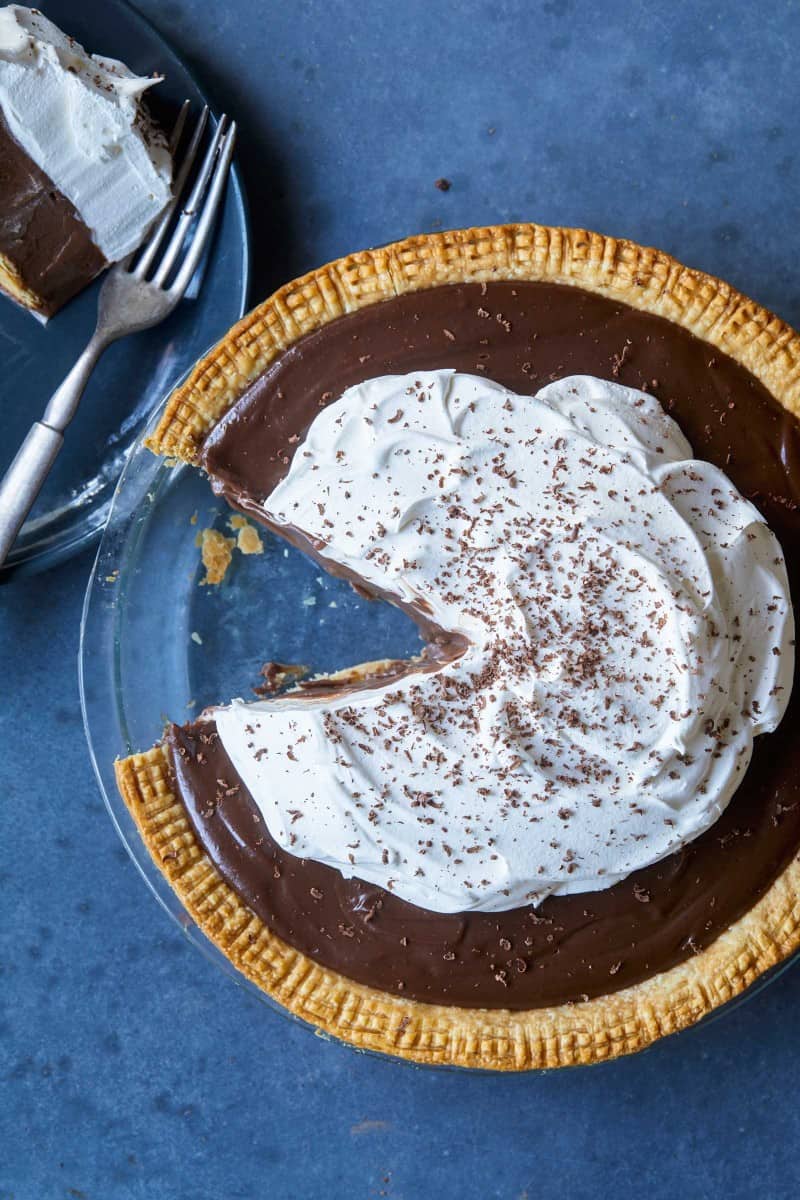 A whole chocolate cream pie with a slice taken out and served with a fork.