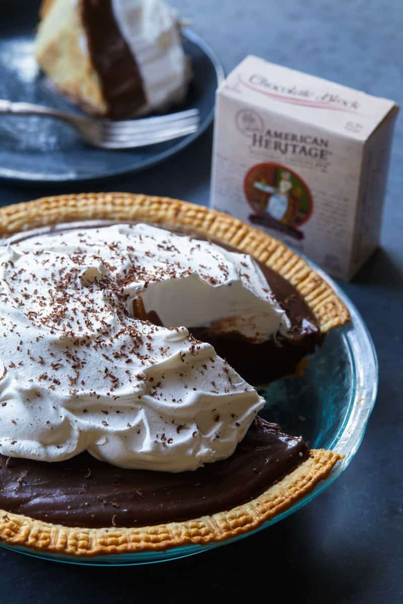 A whole chocolate cream pie with a slice taken out with chocolate drink mix.
