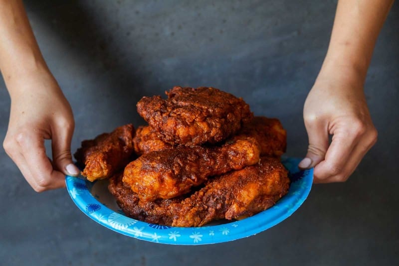 A woman holding a Dixie paper plate of Nashville hot chicken.