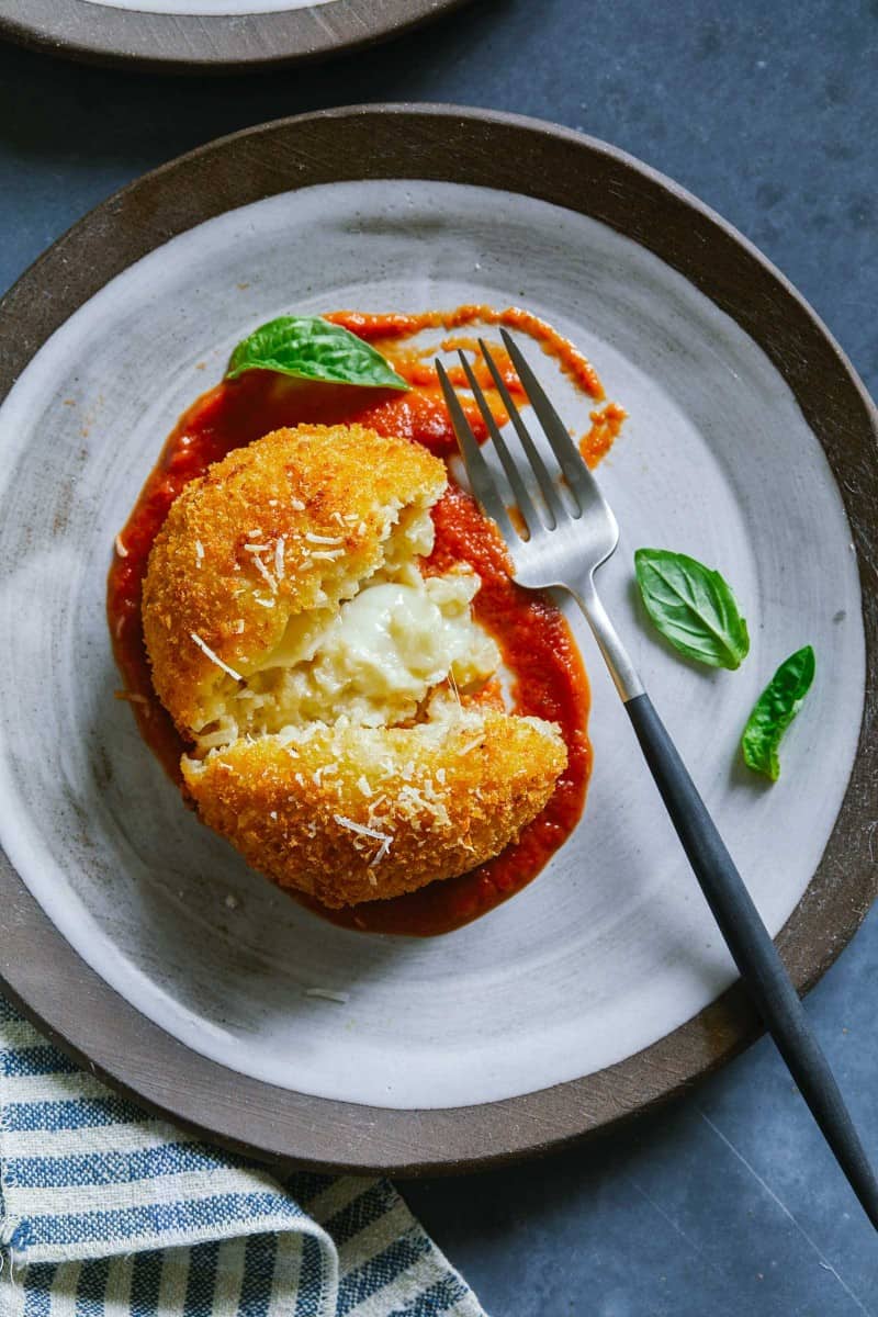 One piece of giant baked cauliflower arancini on a plate with a fork.