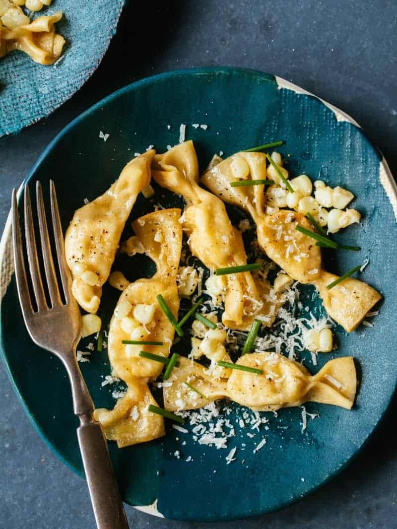 Lobster, corn, and tarragon caramelle on a blue plate with a fork.