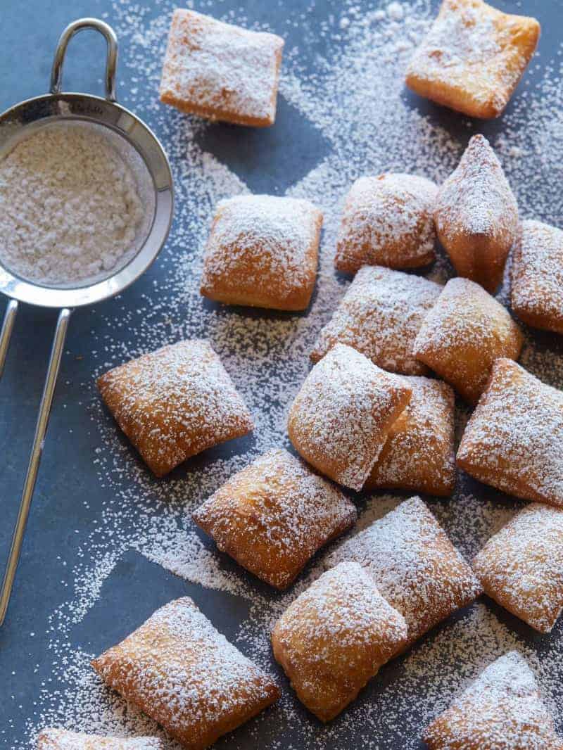 Chai spiced buttermilk beignets covered in powdered sugar with a small sieve.