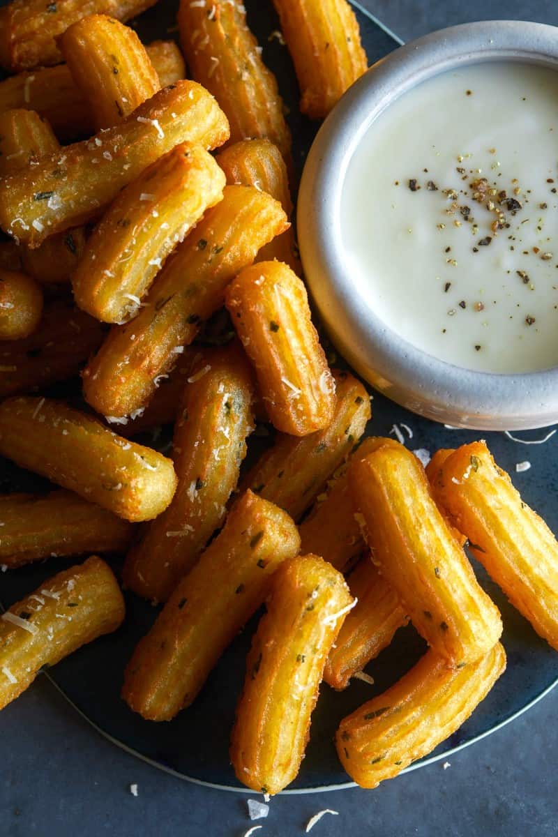 A close up of savory herb churros with white queso dip on the side.