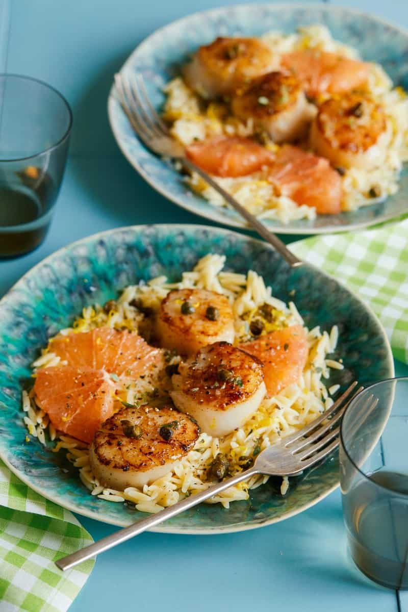 A close up of plates of browned butter seared scallops over lemon orzo with forks.