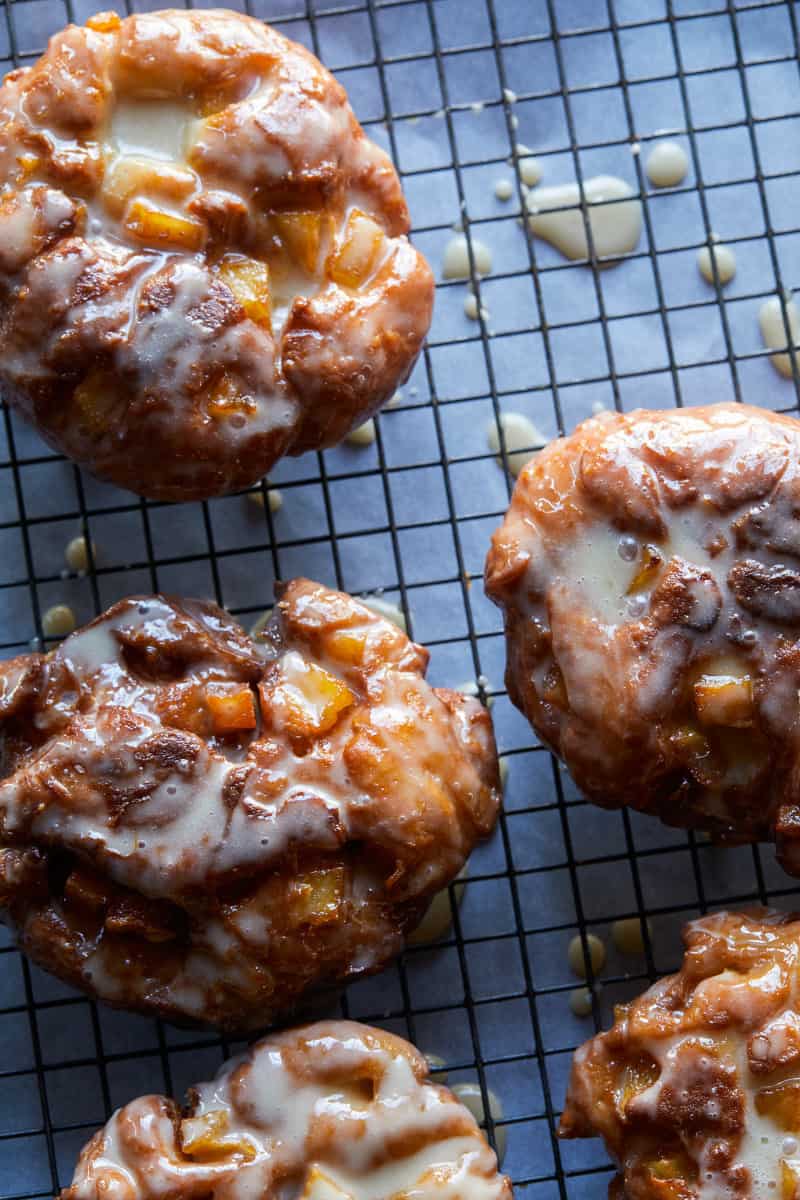 A close up of apple fritters with maple glaze on a cooling rack.