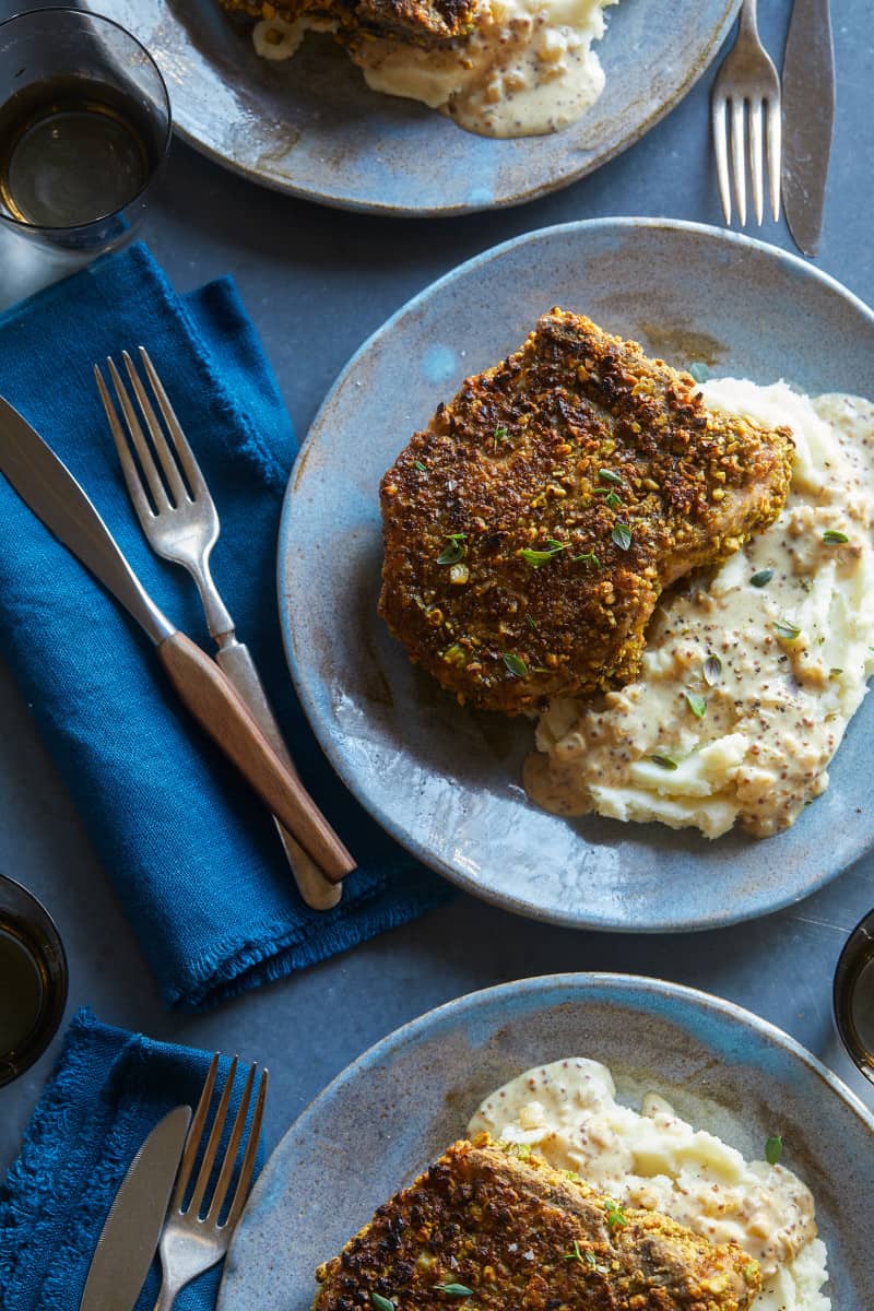 Pistachio crusted pork chop on mashed potatoes with a fork and knife.