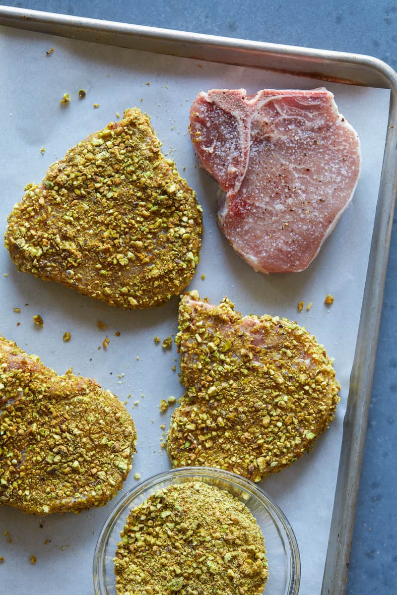 Pistachio crusted raw pork chops on a baking sheet.